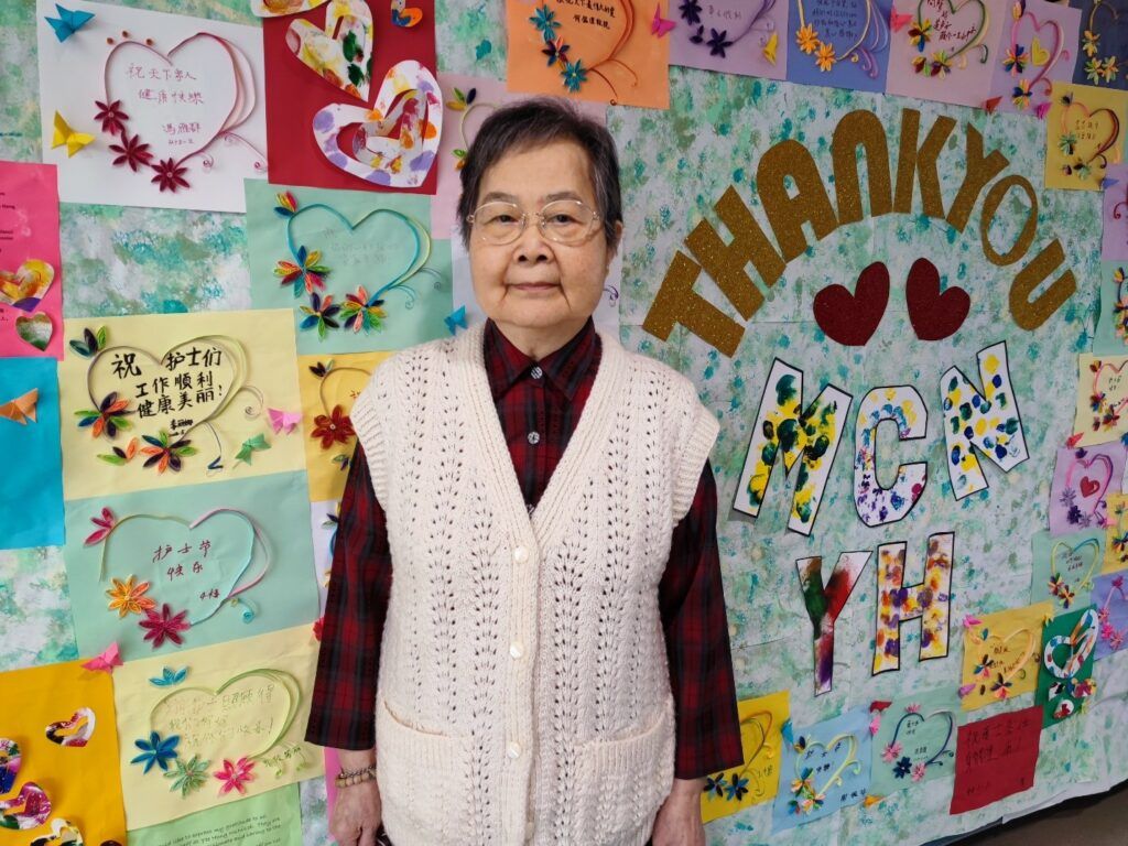 a smiling senior stands in front of a multi-coloured wall decorated with hearts